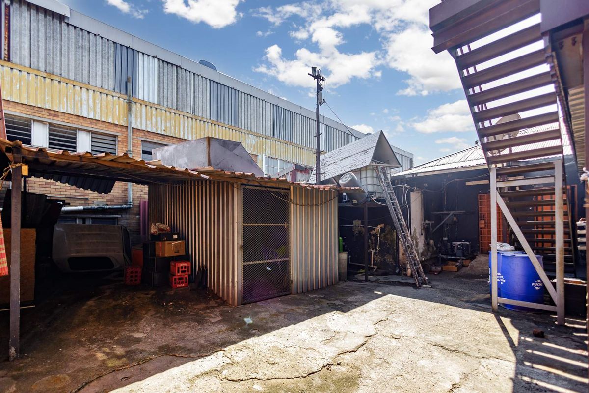 Rear exterior yard area featuring industrial metal structures, concrete paving, and an external metal staircase leading to upper levels.