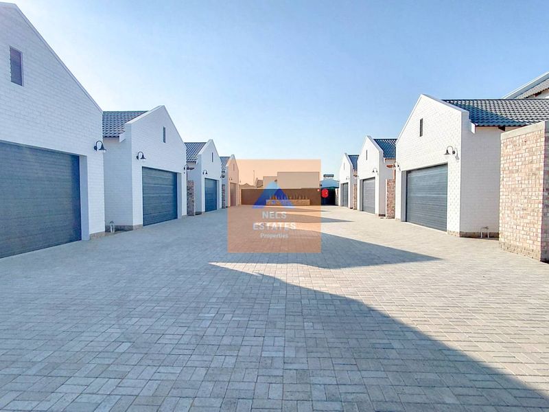 A view of a townhouse complex driveway featuring multiple garage entrances, paved surfaces, and modern white brick facades.