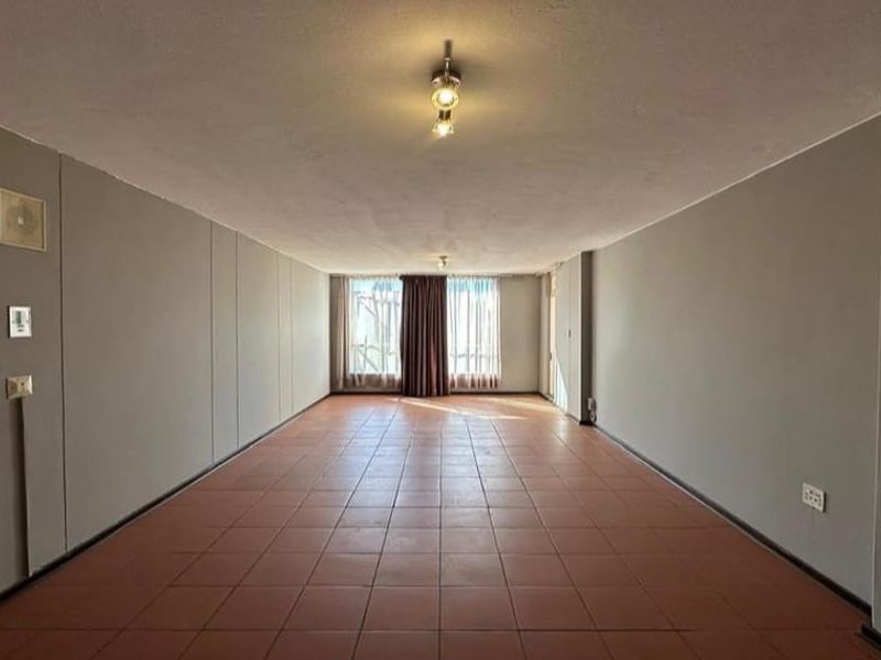 A spacious, empty living area featuring neutral walls, tiled flooring, and a large window allowing natural light to enter the room.