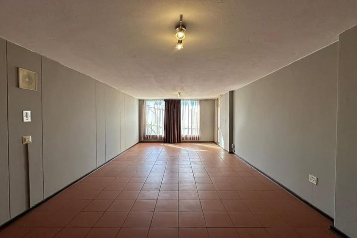 A spacious, empty living area featuring neutral walls, tiled flooring, and a large window allowing natural light to enter the room.