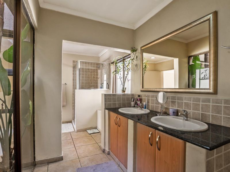 A functional bathroom featuring a double vanity with granite countertops, tiled splashbacks, and a separate shower enclosure with neutral floor tiling.