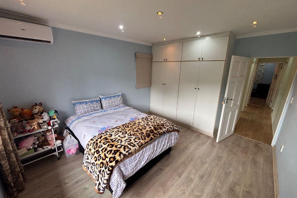 A bedroom featuring built-in floor-to-ceiling wardrobes, laminate wood flooring, recessed ceiling lighting, and a wall-mounted air conditioning unit.
