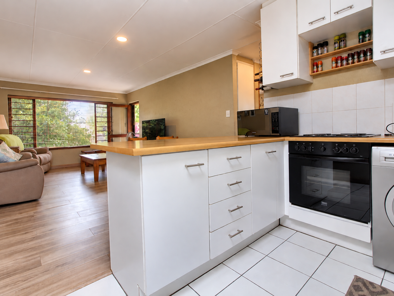 Open-plan kitchen and living area featuring white cabinetry, wooden countertops, built-in oven, and integrated laundry appliances, flowing into a bright lounge space.