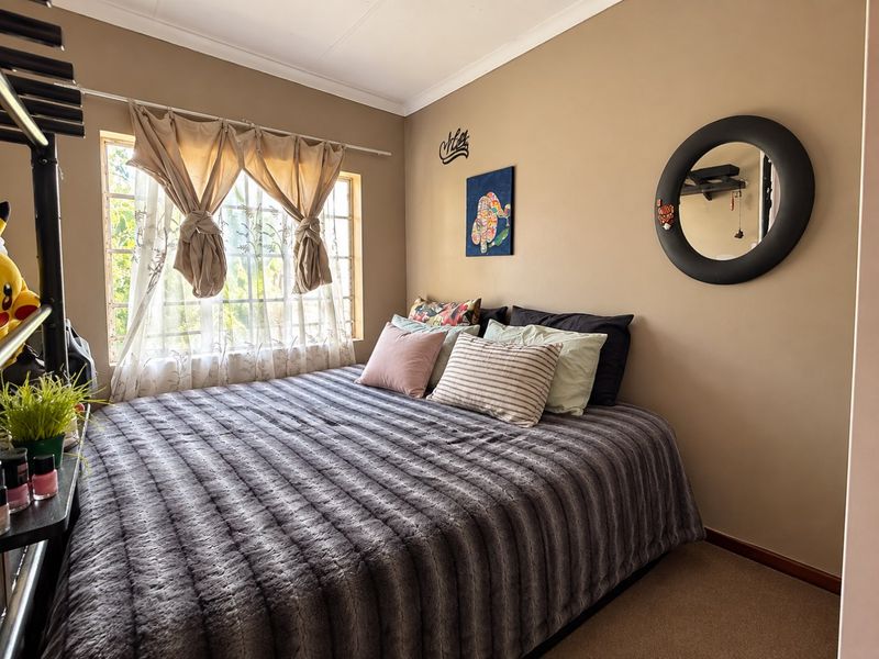 A cozy bedroom featuring carpeted flooring, neutral wall tones, and a window fitted with security burglar bars.