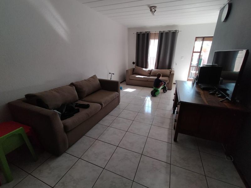A spacious living room featuring tiled flooring and timber-look ceiling panels, with direct access to an outdoor area through a glass panel door.