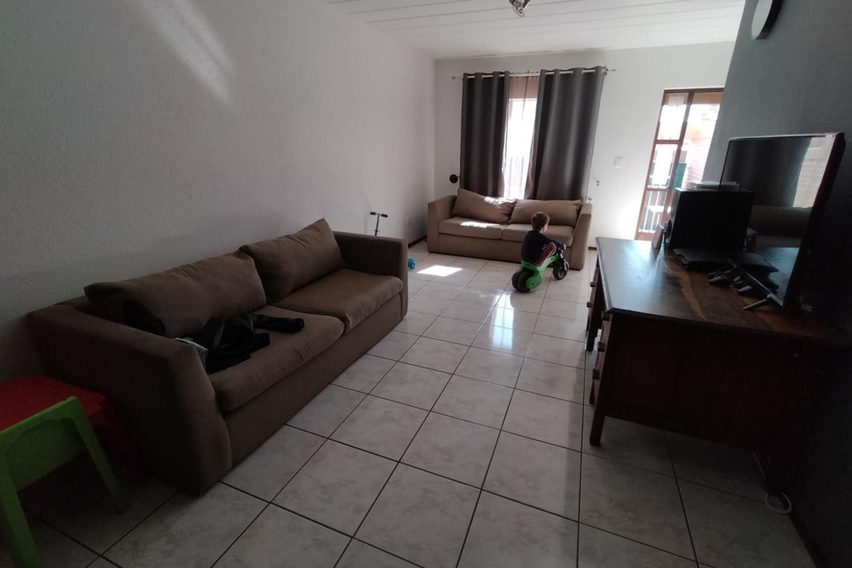 A spacious living room featuring tiled flooring and timber-look ceiling panels, with direct access to an outdoor area through a glass panel door.