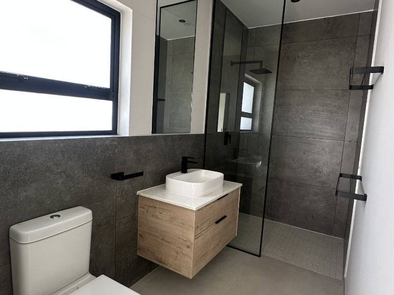 Modern bathroom featuring a floating vanity, vessel sink, walk-in shower with glass screen, and contemporary grey tiling throughout.