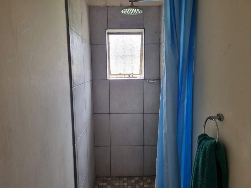 A functional shower enclosure featuring tiled walls, a fixed shower head, and an obscured glass window for privacy.