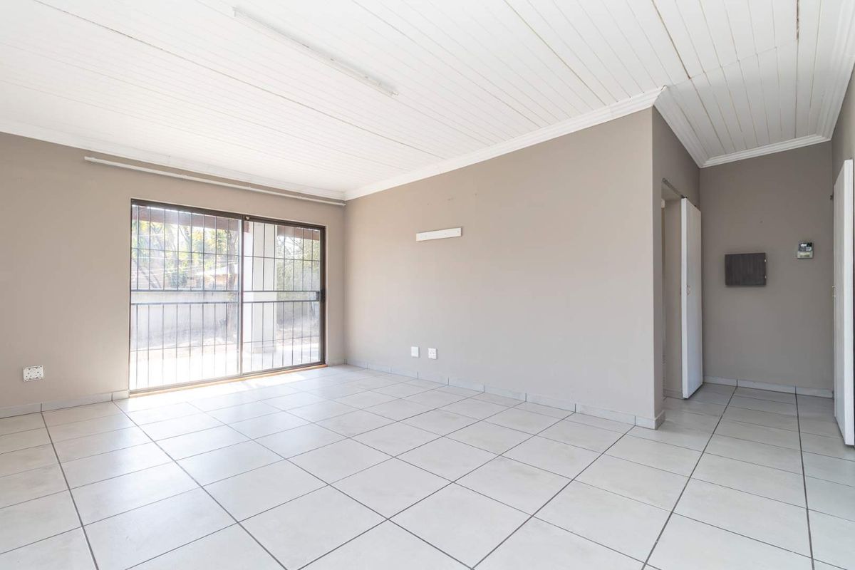 A bright, empty living room featuring neutral tiled flooring, a white tongue-and-groove ceiling, and sliding glass doors leading to the exterior.