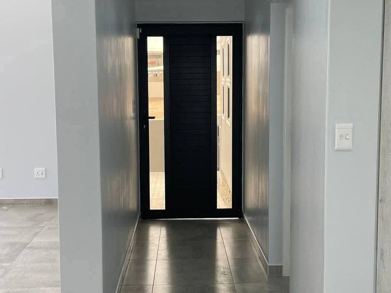 A clean, modern entrance hall featuring large format floor tiles, recessed downlighting, and a contemporary dark-framed front door with glass side panels.