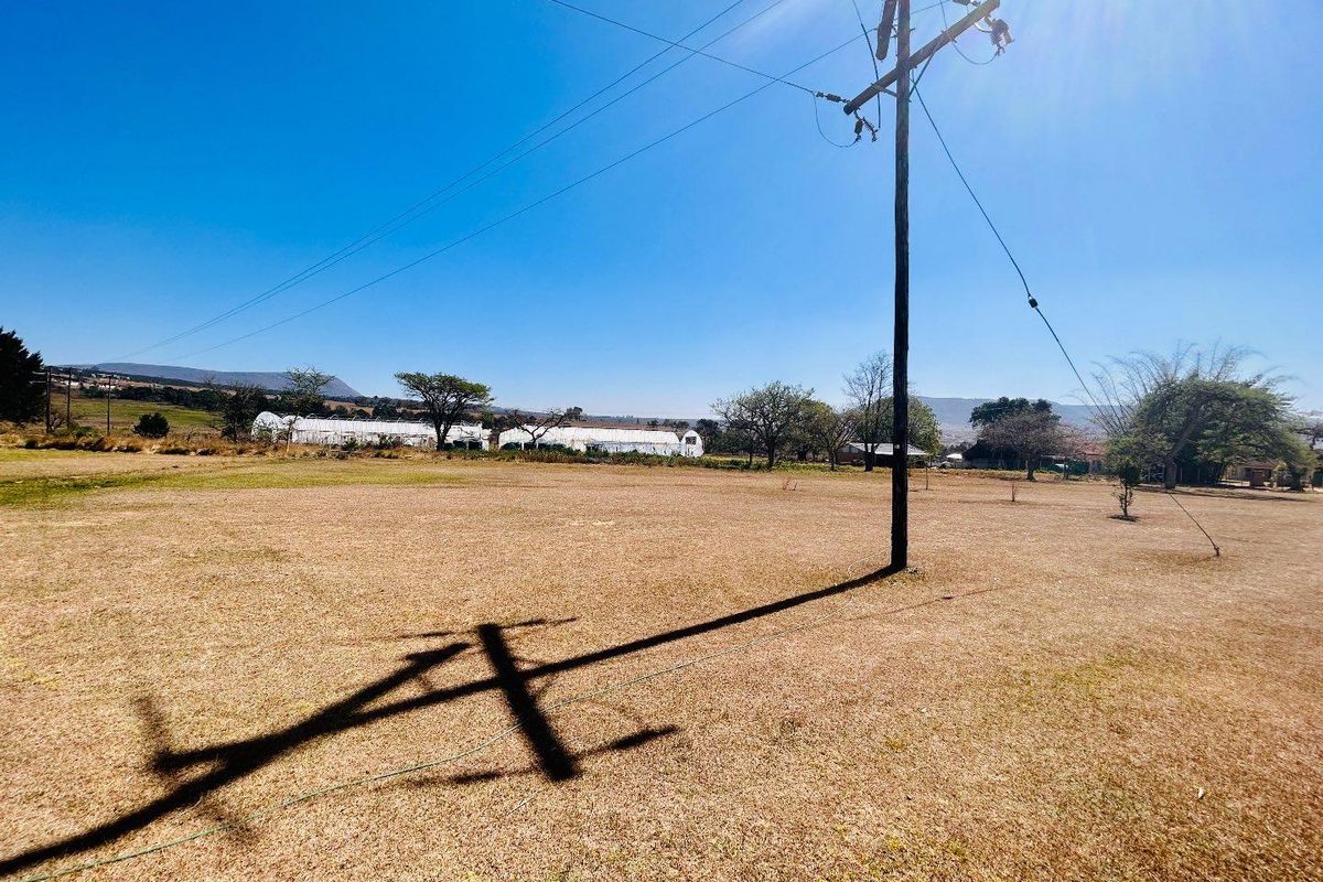 Expansive open land area featuring a utility pole and distant agricultural structures under a clear blue sky.