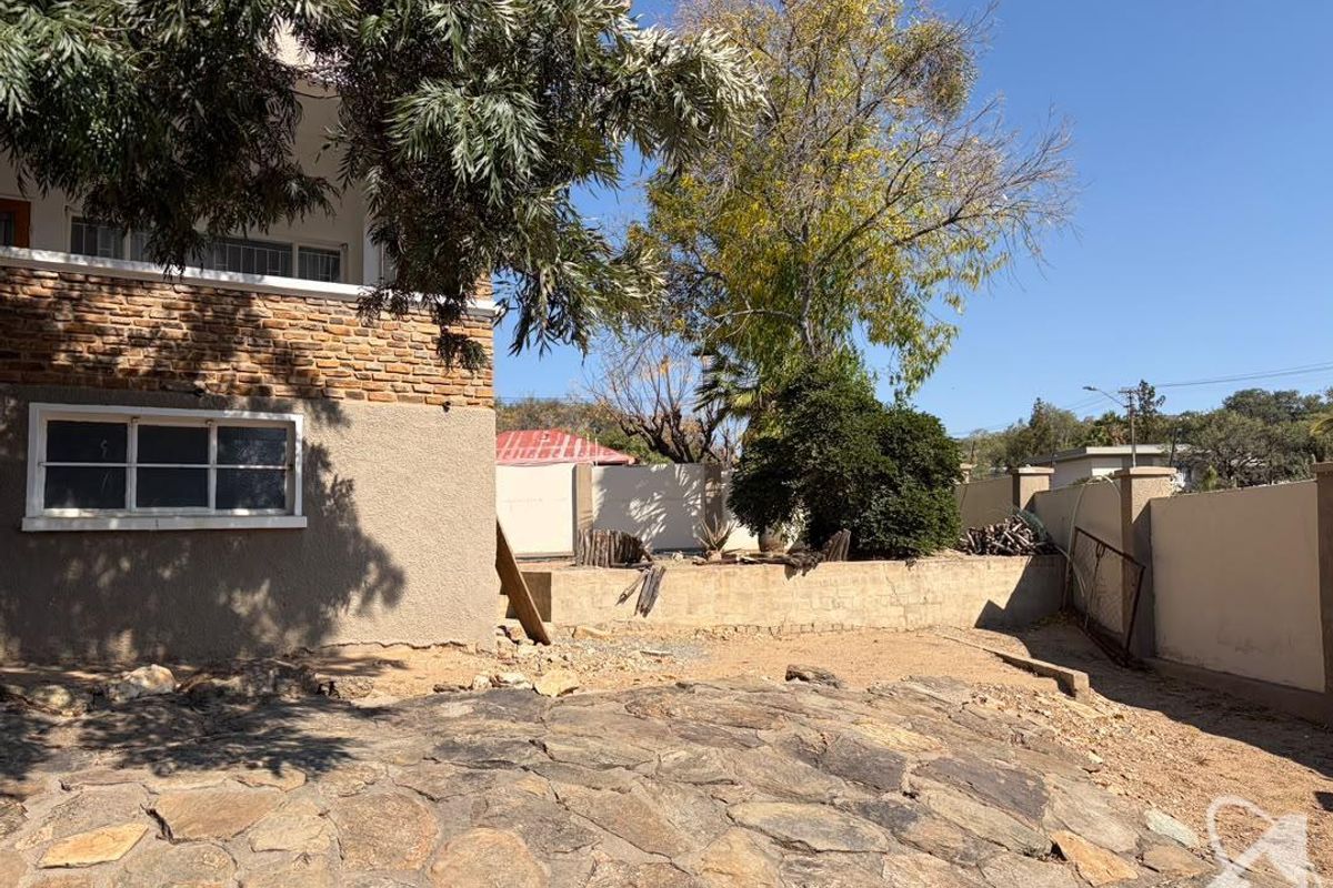 Rear exterior area featuring stone paving, a brick facade, and a boundary wall, requiring landscaping and surface improvements.