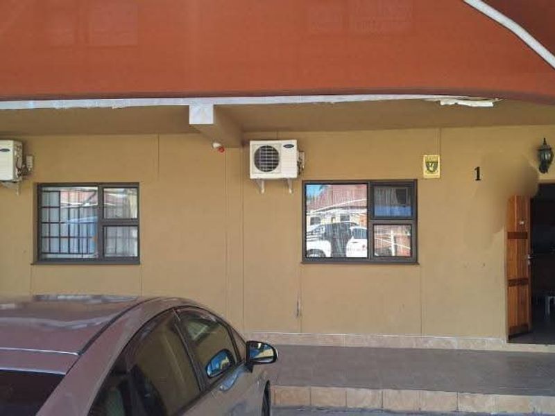 Front exterior view of the apartment entrance featuring a covered parking area, security bars on windows, and wall-mounted air conditioning units.