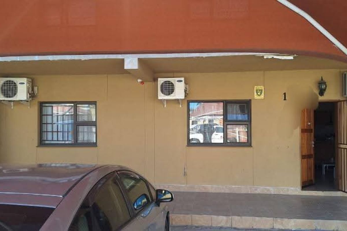 Front exterior view of the apartment entrance featuring a covered parking area, security bars on windows, and wall-mounted air conditioning units.