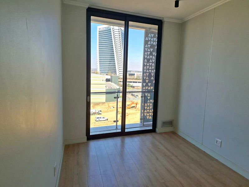 A bright, empty bedroom featuring modern laminate flooring and a large sliding glass door leading to a balcony with a decorative privacy screen.