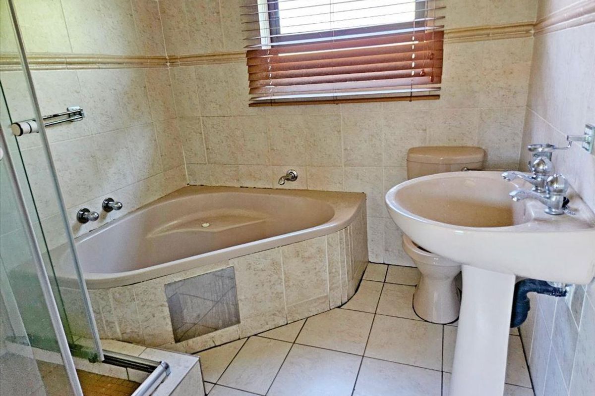 A dated bathroom featuring a corner bathtub, pedestal basin, toilet, and separate shower enclosure with neutral wall and floor tiling.