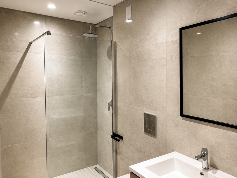 Modern bathroom featuring a walk-in shower with glass screen, rain shower head, wall-mounted flush plate, and a sleek vanity basin with a framed mirror.