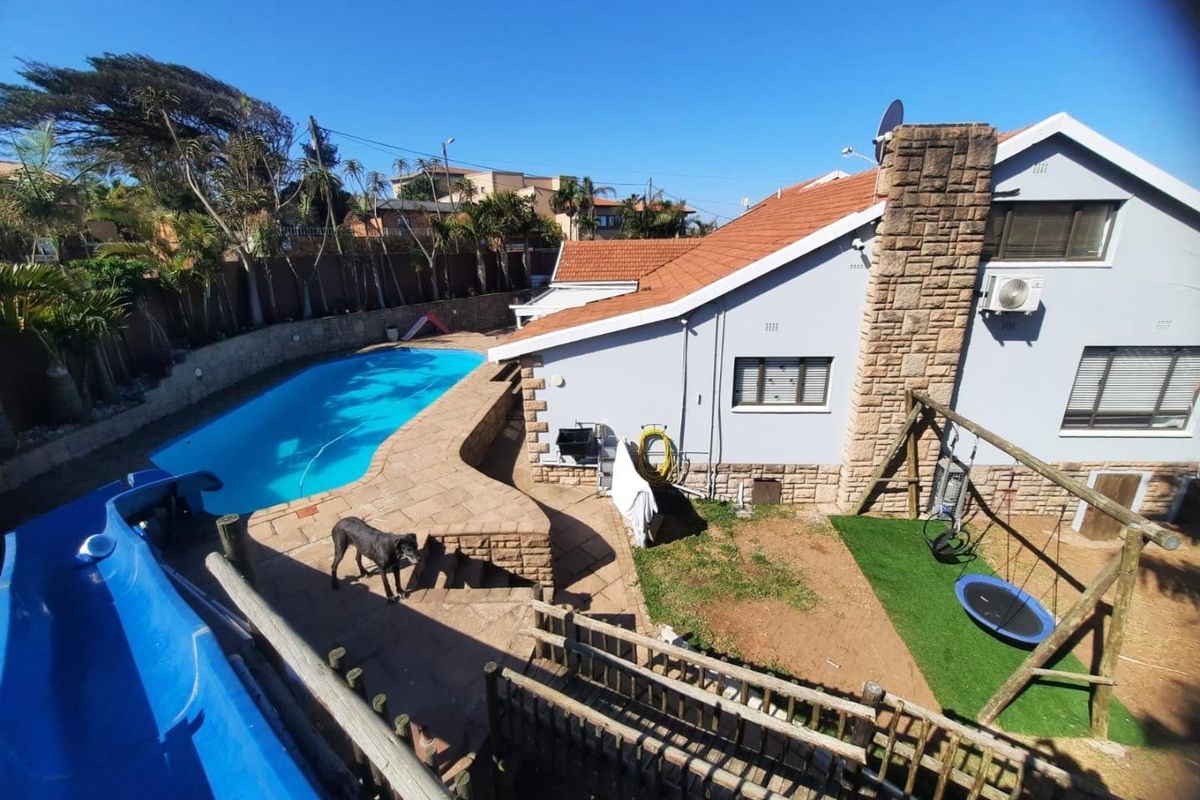 Rear exterior view featuring a swimming pool, paved patio area, stone chimney feature, and a landscaped garden with artificial grass.