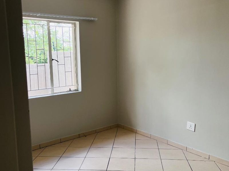 A clean, empty bedroom featuring neutral wall paint, tiled flooring, and a window fitted with security bars.