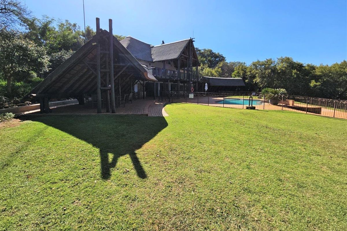 A spacious rear garden featuring a swimming pool with safety fencing and a large thatched-roof patio area, ideal for outdoor entertaining.