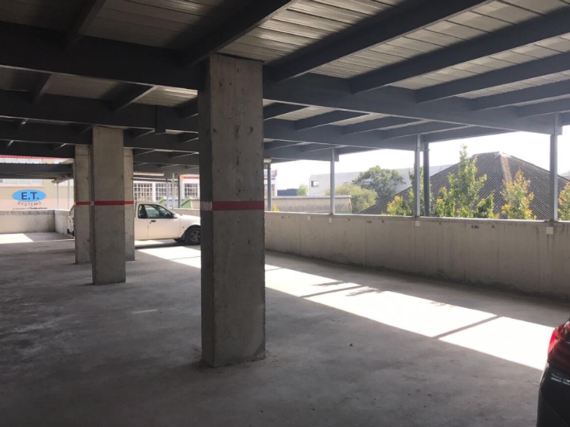 A covered, open-plan parking garage featuring exposed steel roof beams and concrete structural columns.
