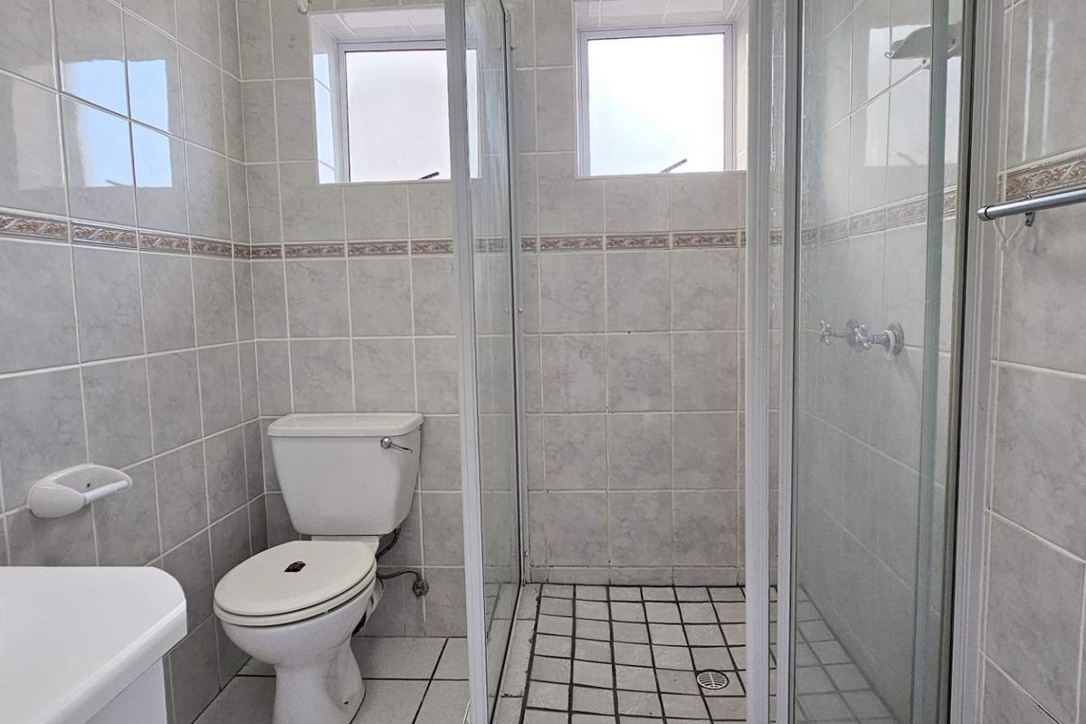 A functional bathroom featuring a glass-enclosed shower, tiled walls, and standard sanitary fixtures, providing a clean and practical space.