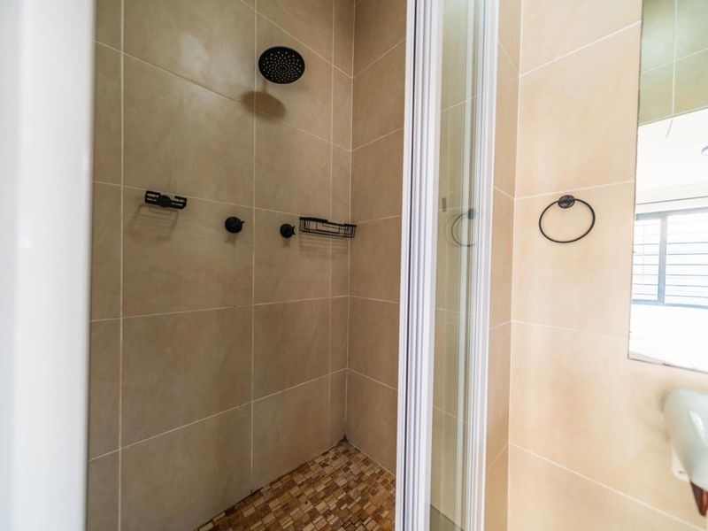 A clean, modern bathroom shower enclosure featuring neutral wall tiles, a rainfall shower head, and a glass door.