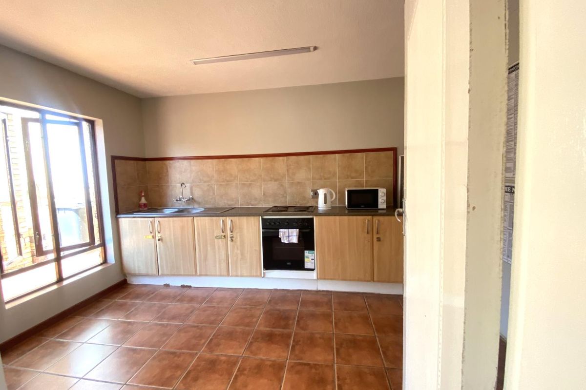 A functional kitchen featuring light wood cabinetry, a built-in oven and hob, tiled backsplash, and ceramic floor tiles with natural light from a large window.