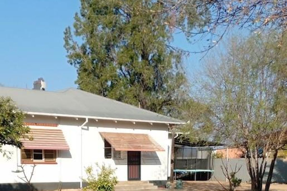 Rear view of the house featuring a metal roof, window awnings, and a security gate, set within a spacious, low-maintenance garden area.