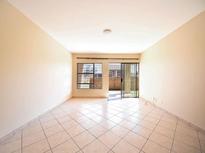 An empty, open-plan living area featuring neutral tiled flooring, a sliding door leading to the exterior, and a window with security bars.