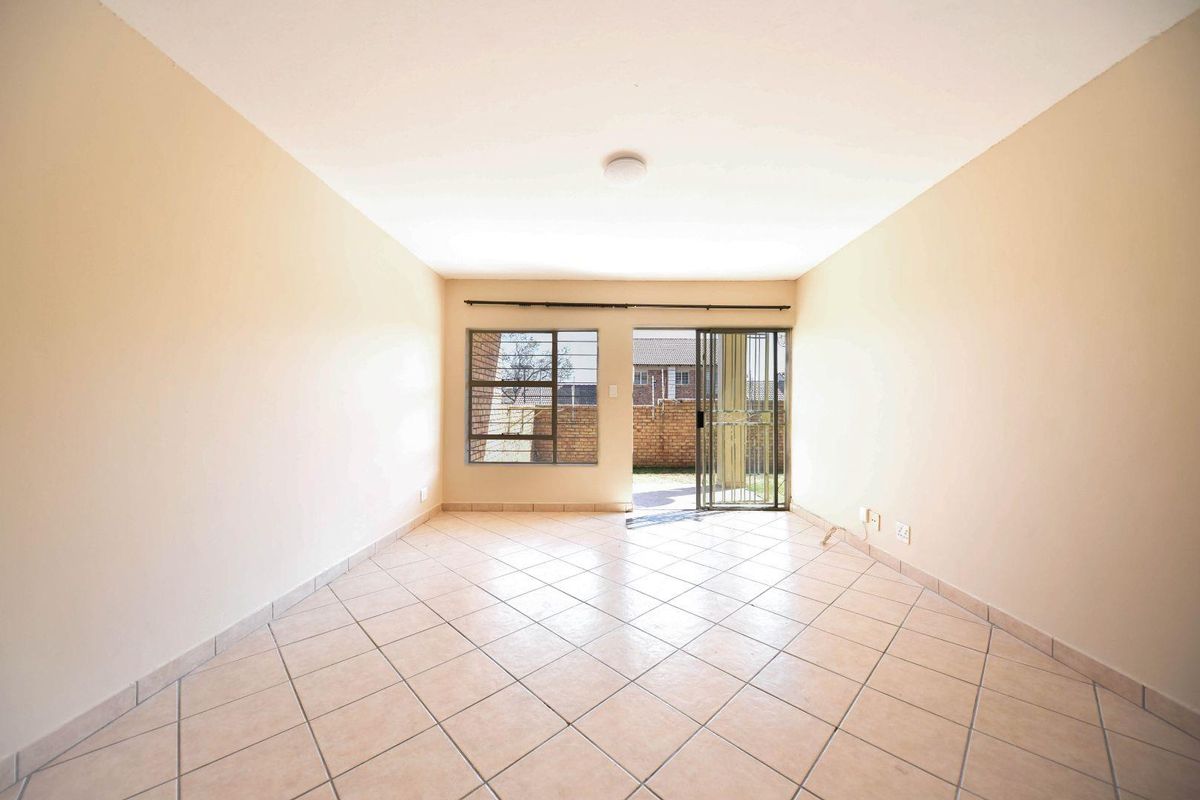 An empty, open-plan living area featuring neutral tiled flooring, a sliding door leading to the exterior, and a window with security bars.
