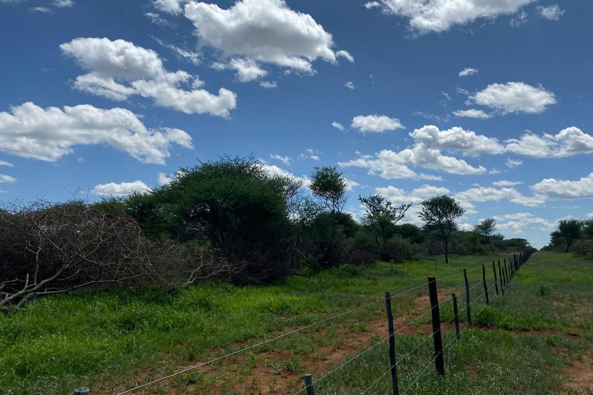 An expansive outdoor view of the small holding featuring natural vegetation, open green space, and perimeter wire fencing with wooden posts.