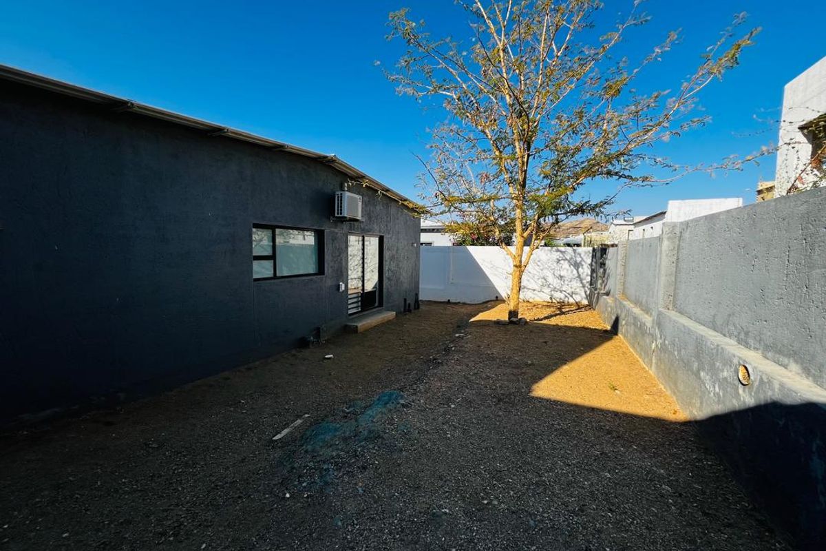A rear exterior view of the property featuring a gravel yard, boundary walls, and a sliding door access point.