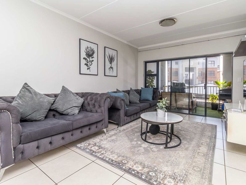 A bright and well-maintained living room featuring neutral tiled flooring and large sliding glass doors that provide access to an outdoor balcony area.