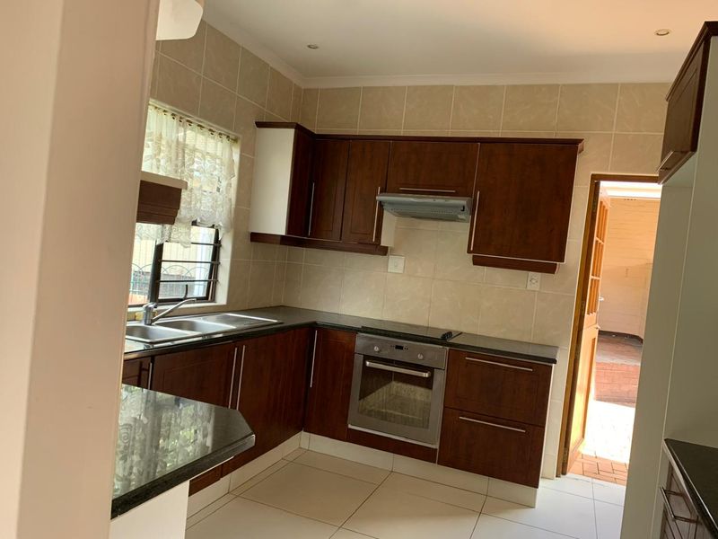 A functional kitchen featuring dark wood cabinetry, granite countertops, built-in oven, hob, and extractor fan, with neutral tiled splashbacks and flooring.