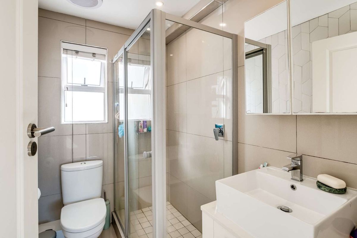 Modern bathroom featuring a glass-enclosed shower, wall-mounted vanity with basin, and a toilet, finished with neutral wall tiles.
