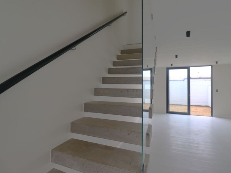 Modern interior featuring a minimalist concrete floating staircase with a glass balustrade, leading to an open-plan living area with access to an outdoor space.