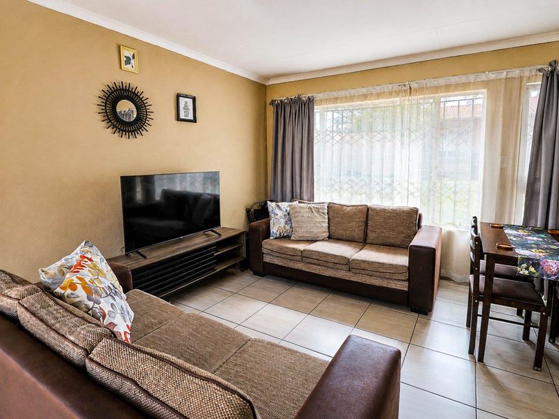 A comfortable living room featuring tiled flooring and a large window with a security gate, providing natural light to the space.