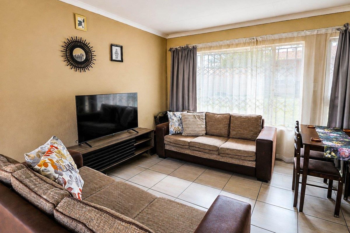 A comfortable living room featuring tiled flooring and a large window with a security gate, providing natural light to the space.