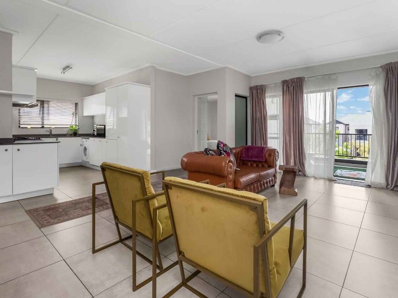 An open-plan living area featuring tiled floors, a modern kitchen with built-in cabinetry, and direct access to a balcony through sliding glass doors.