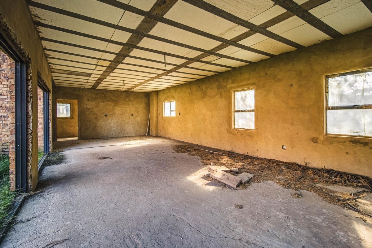 An unfinished, open-plan interior space featuring exposed ceiling beams, concrete flooring, and large sliding doors, offering a blank canvas for renovation.