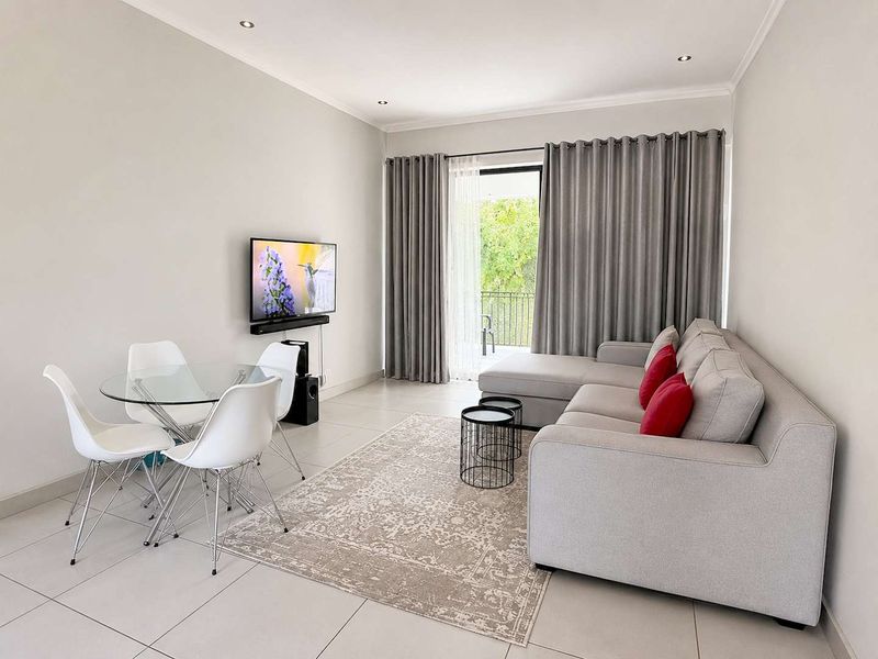 A bright open-plan living and dining area featuring neutral tiled flooring, recessed lighting, and direct access to a balcony through sliding glass doors.
