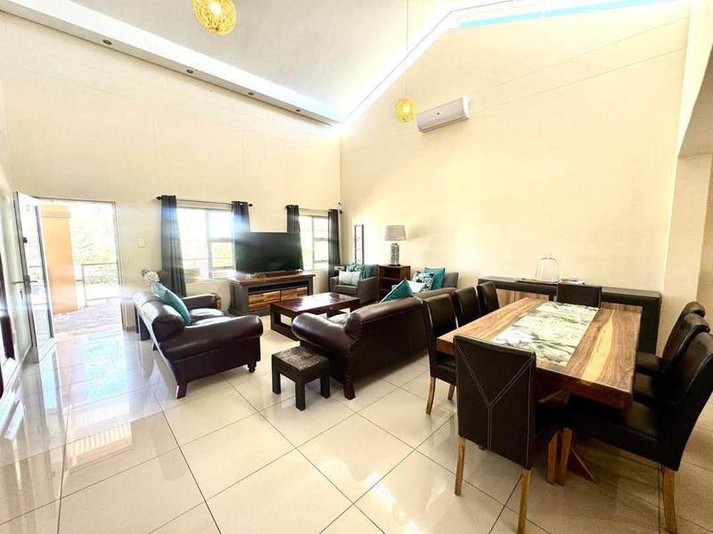 Spacious open-plan living and dining area featuring high vaulted ceilings, polished tile flooring, and a wall-mounted air conditioning unit.