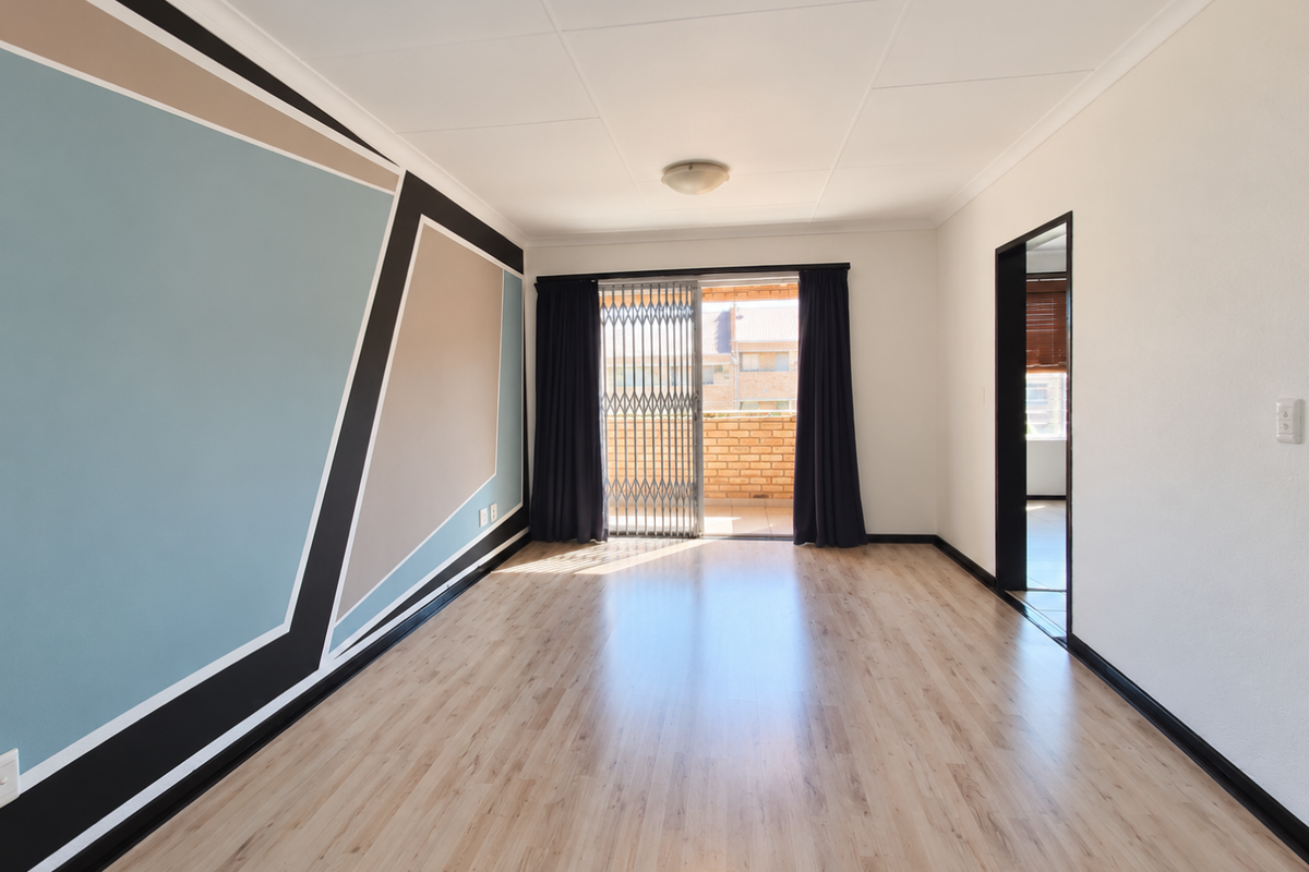 A bright, empty living room featuring light-toned laminate flooring, a decorative geometric accent wall, and a sliding door leading to an outdoor balcony.