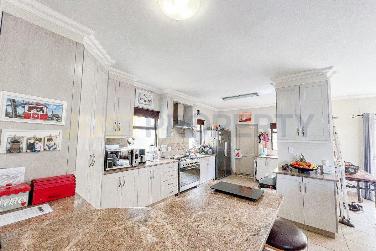 A well-appointed kitchen featuring granite countertops, light-toned cabinetry, a built-in oven with extractor fan, and a breakfast bar island.