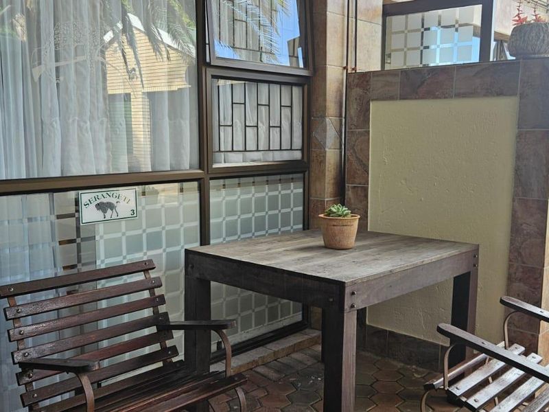 A covered patio area featuring tiled flooring, stone-look wall cladding, and large aluminium-framed windows with security bars.