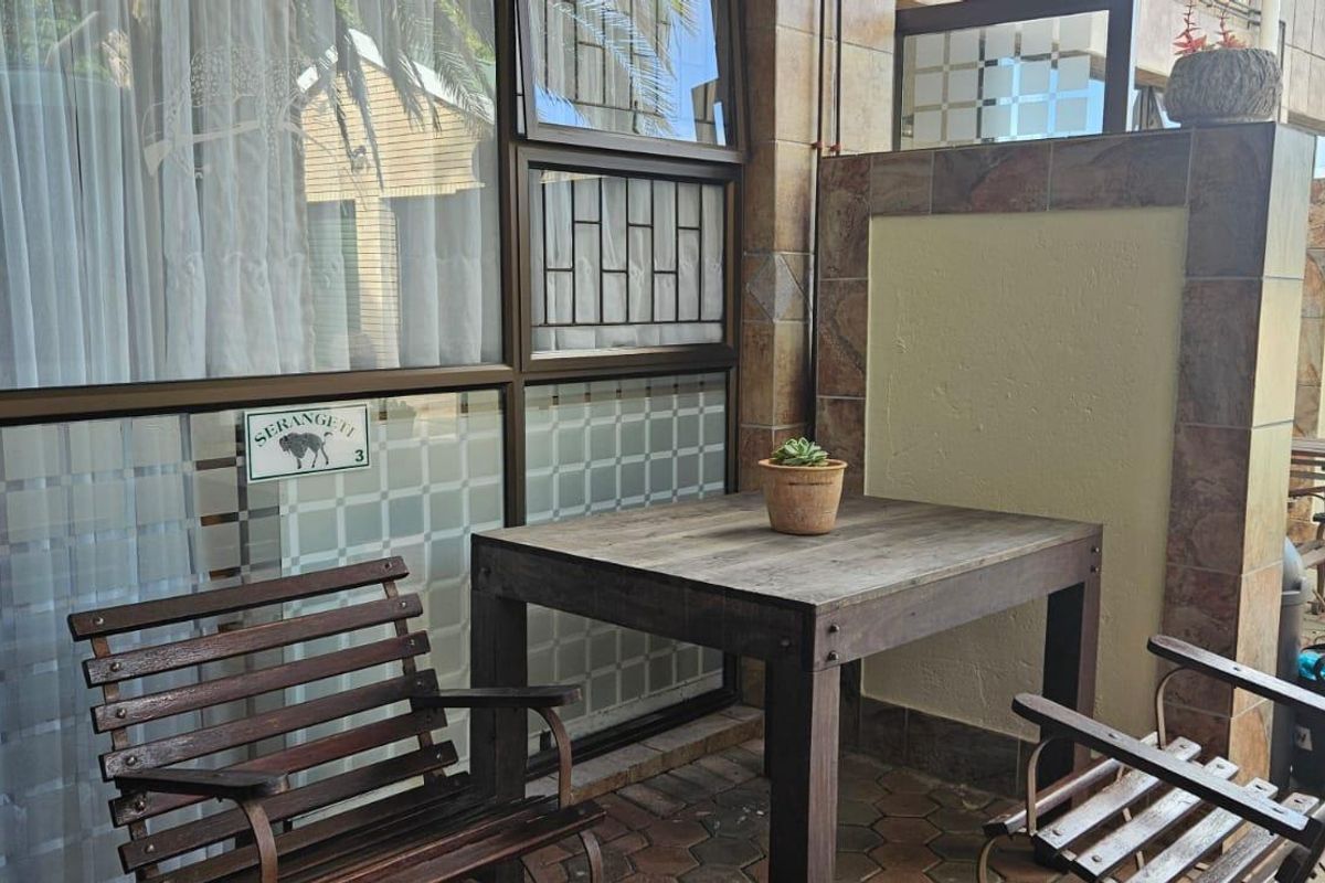 A covered patio area featuring tiled flooring, stone-look wall cladding, and large aluminium-framed windows with security bars.