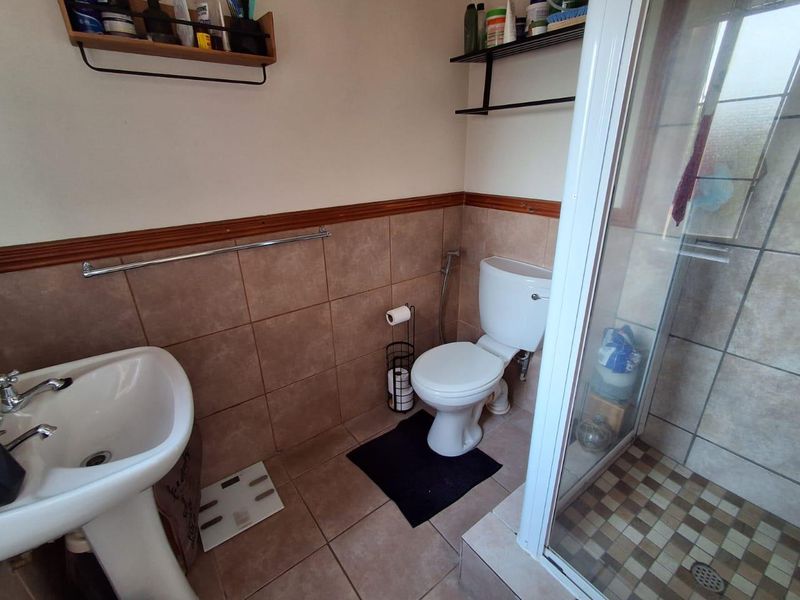 A functional bathroom featuring a pedestal basin, toilet, and a glass-enclosed shower with tiled finishes.