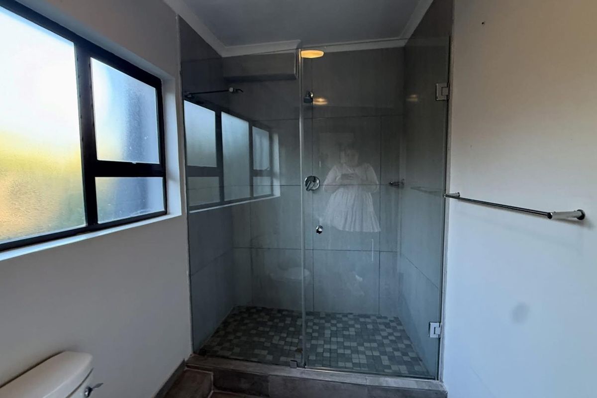 A clean bathroom featuring a glass-enclosed shower with mosaic floor tiling, a wall-mounted towel rail, and a window for natural light.