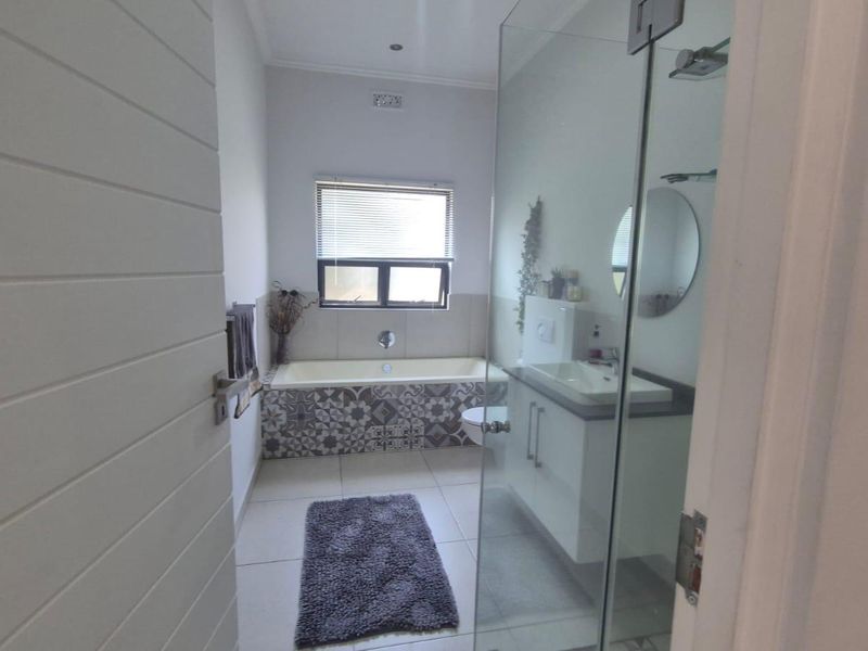 Modern bathroom featuring a glass-enclosed shower, a vanity with basin, and a bathtub with decorative patterned tiling.
